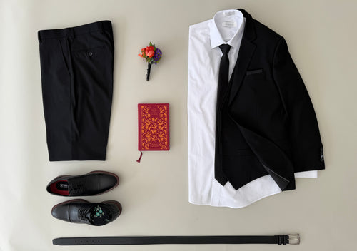 Studio picture of black vested suit, white dress shirt, black tie, black pocket square, black dress shoes and black belt.