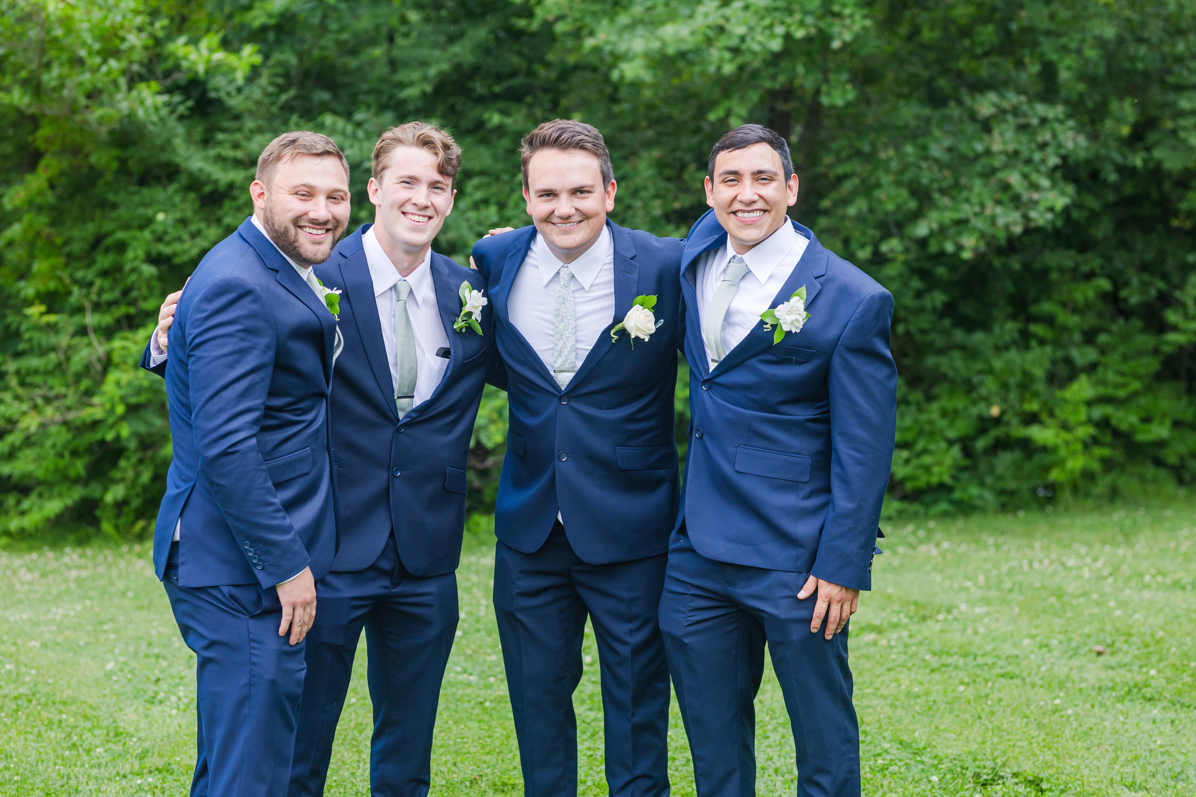 Groom and 3 groomsmen standing outdoors wearing cobalt blue suits, white dress shirts, and ties.