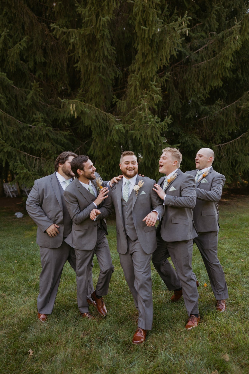 Groom and groomsmen wearing vested medium grey suits, white dress shirt, light color tie and cognac shoes.