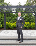 Handsome groom wearing a vested charcoal grey suit, white shirt, white bowtie, white pocket square, black dress shoes and black belt