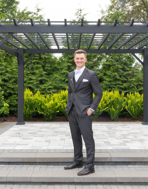 Handsome groom wearing a vested charcoal grey suit, white shirt, white bowtie, white pocket square, black dress shoes and black belt
