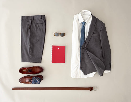 Studio picture of a medium grey vested suit, white dress shirt, blue tie, cognac dress shoes and cognac belt.