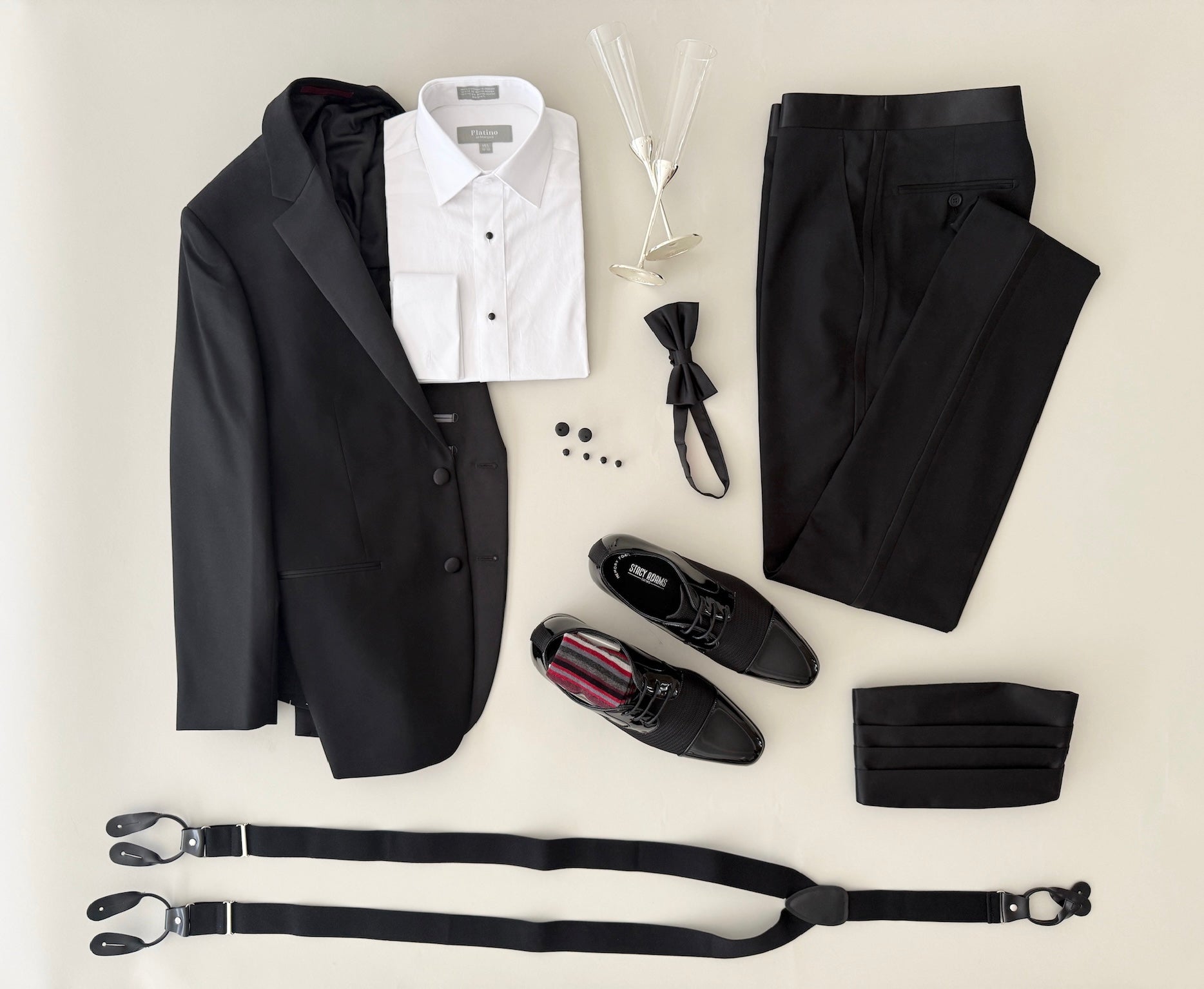 studio shot of a black notch lapel tuxedo, no pleat formal shirt, black bowtie and cummerbund set, silver cufflinks and studs, black leather trim suspenders and fashion black patent leather and woven fabric formal shoes.