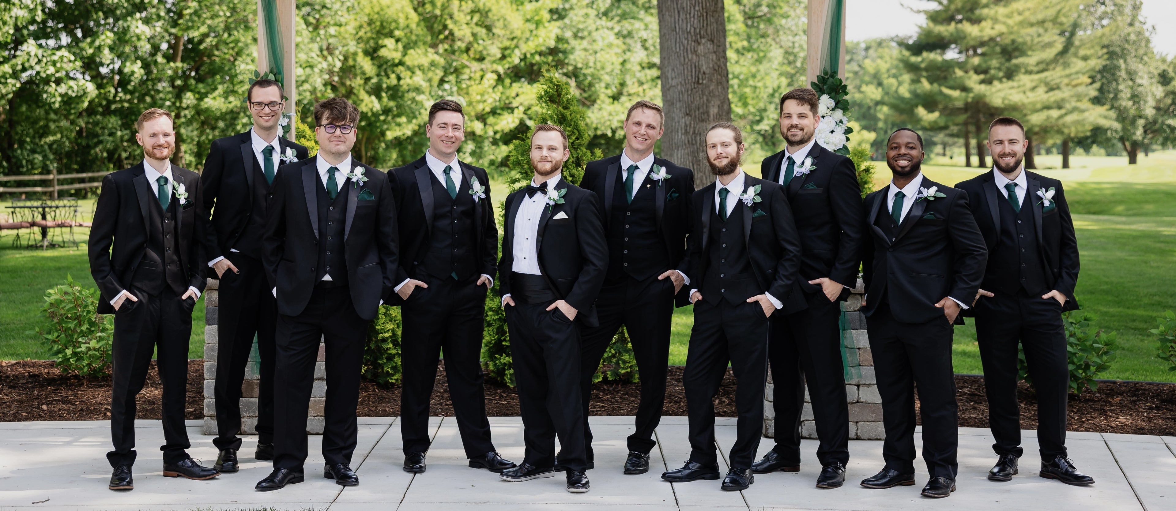 Large group of men wearing black tuxedos.  Diverse group of different sizes encouraging the user to click through for measurement guidelines.